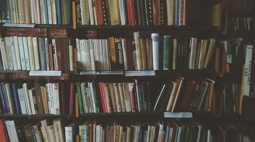 A close up shot of a bookshelf that is full of various books.